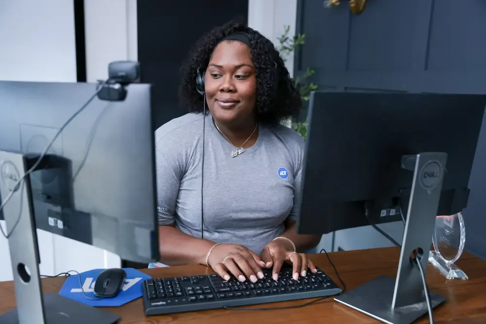 An ADT employee wearing a headset and smiling while working at a dual-monitor desk setup.