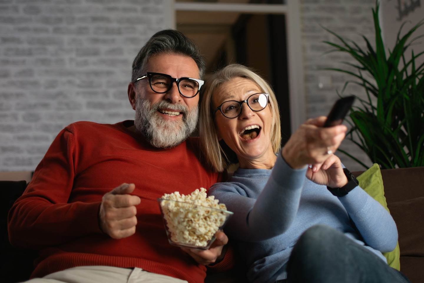 Senior couple laughing, eating popcorn, and watching their favorite TV show.
