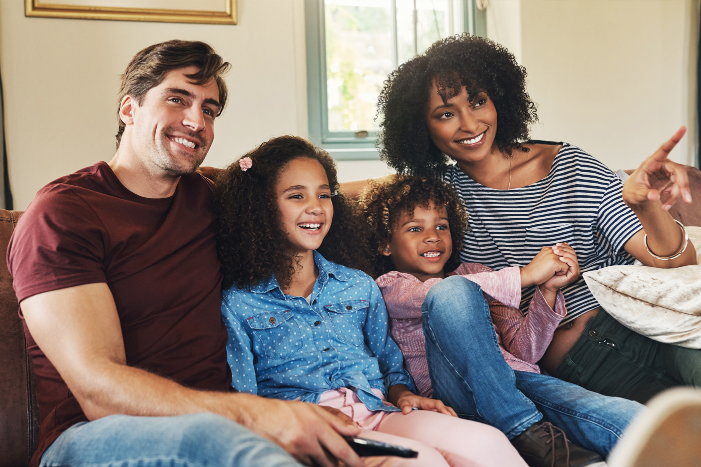 Mixed race family (mom, dad, and two daughters) watching tv in the living room