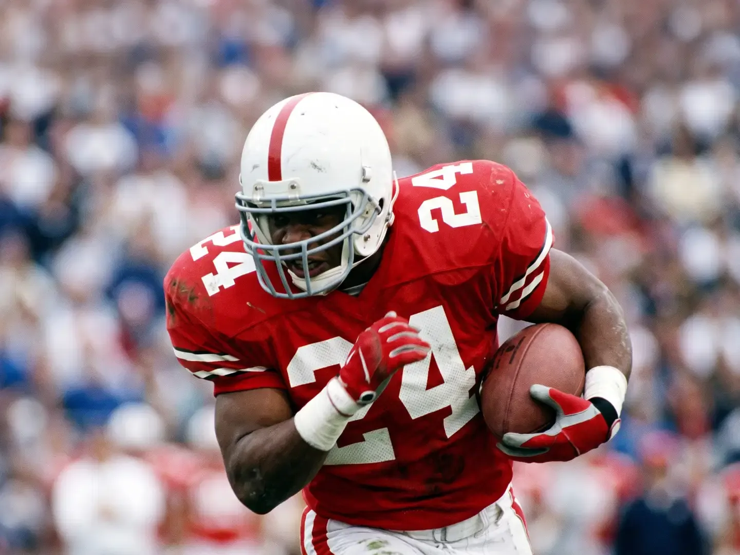 An American football player wearing a red and white helmet and jersey runs with the ball during a game.