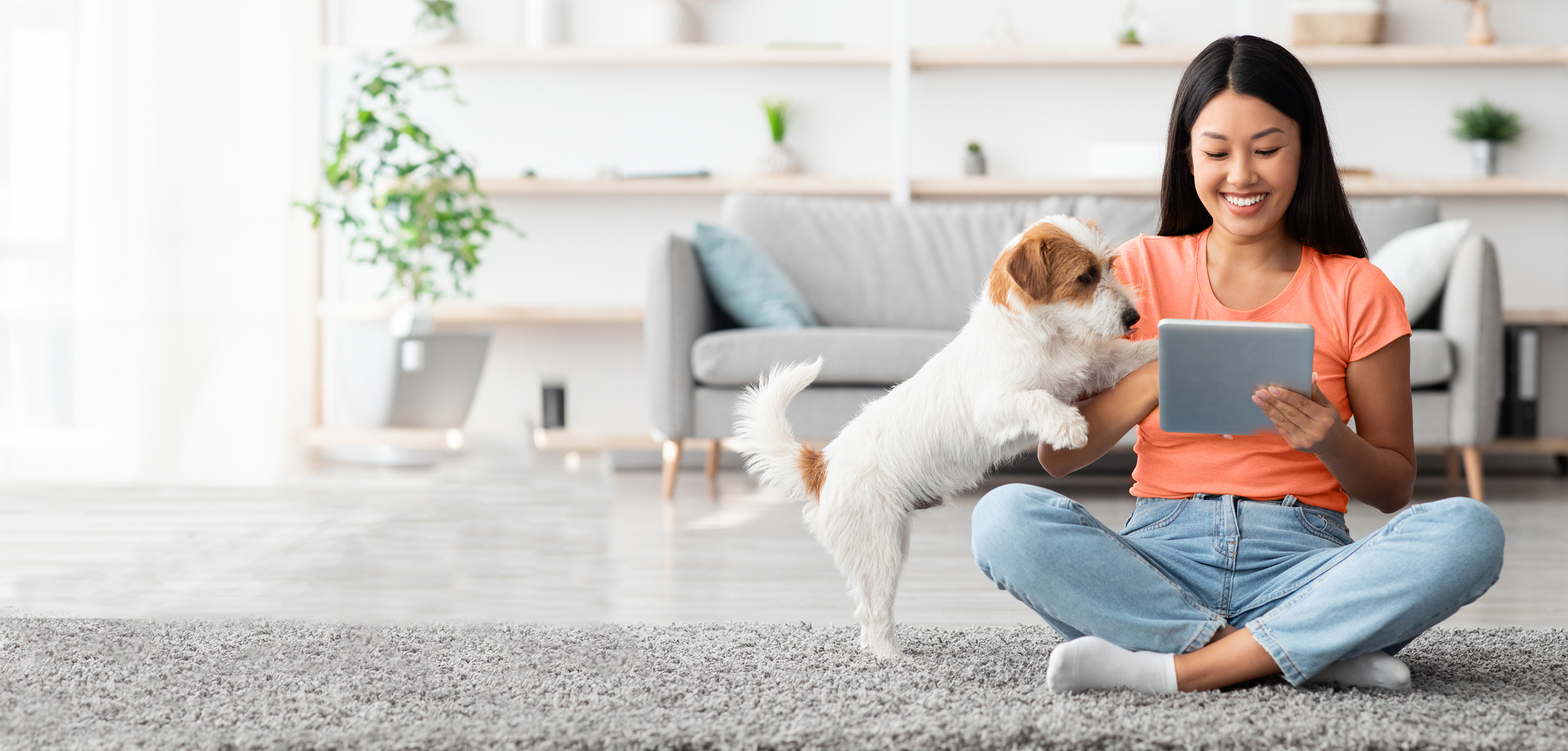 Chica con un perro sentado en la alfombra y mirando una tableta