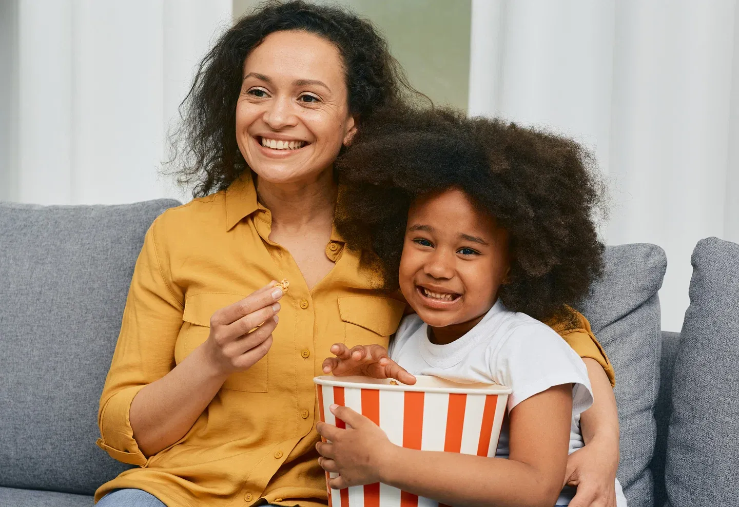 Madre e hija viendo películas y comiendo palomitas de maíz en su sofá gris. Mother and Daughter Watching movie and eating popcorn on their grey sofa.