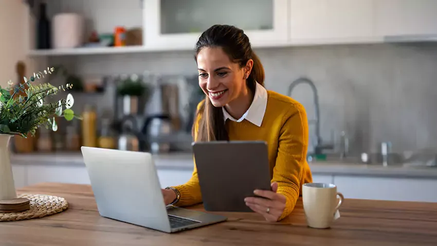 Happy woman uses laptop and tablet with fast internet at home.