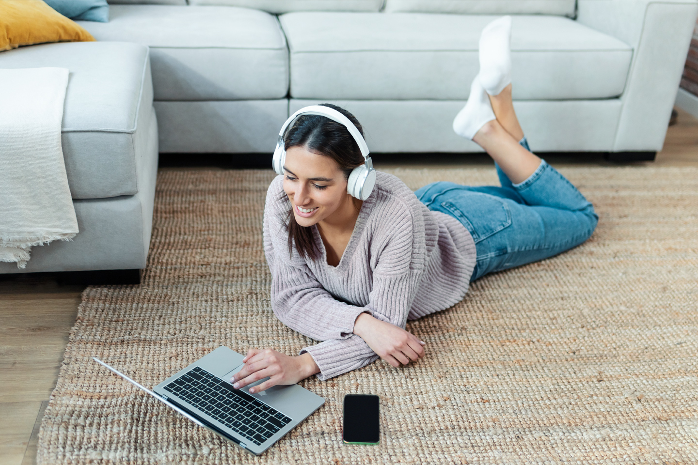 Teen girl wearing headphones laying on floor with laptop and cell phone