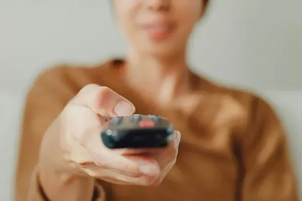 Blurred out image of woman pointing a remote towards a TV