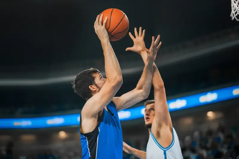 Two male basketball players contesting a shot at an indoor arena.