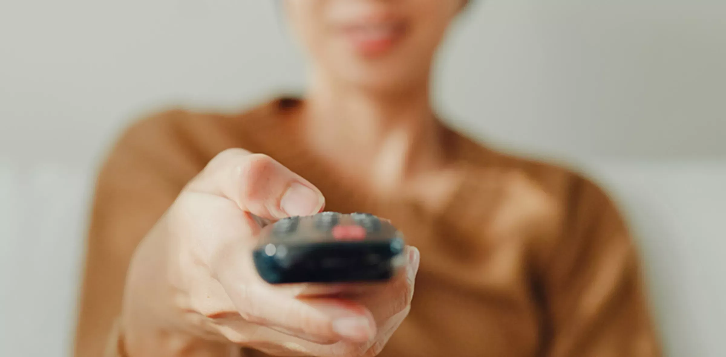 Blurred out image of woman pointing a remote towards a TV