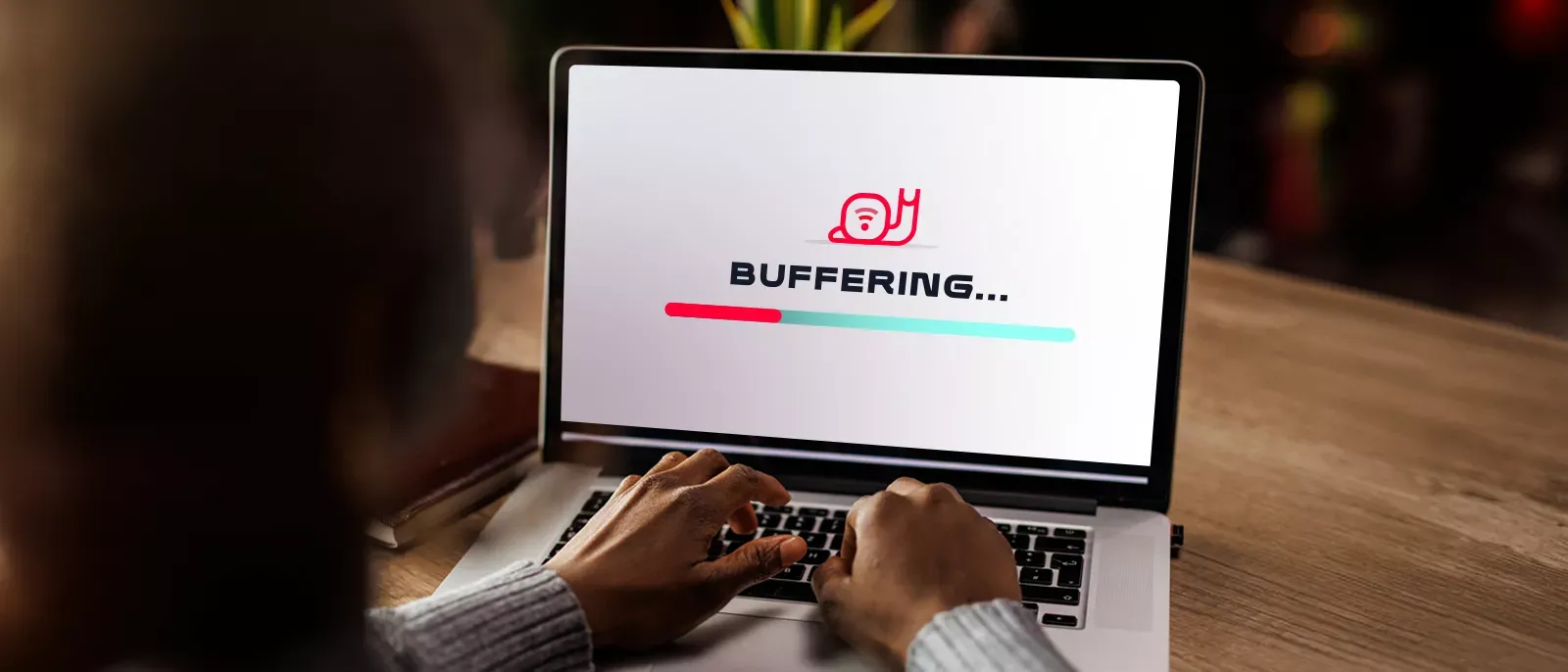 Hands at a computer. Image on the screen is a snail icon saying buffering. The image represents slow internet.