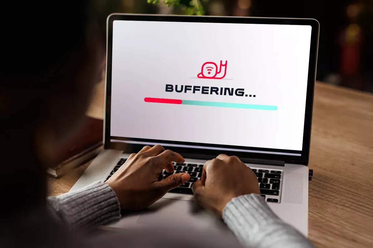 Hands at a computer. Image on the screen is a snail icon saying buffering. The image represents slow internet.