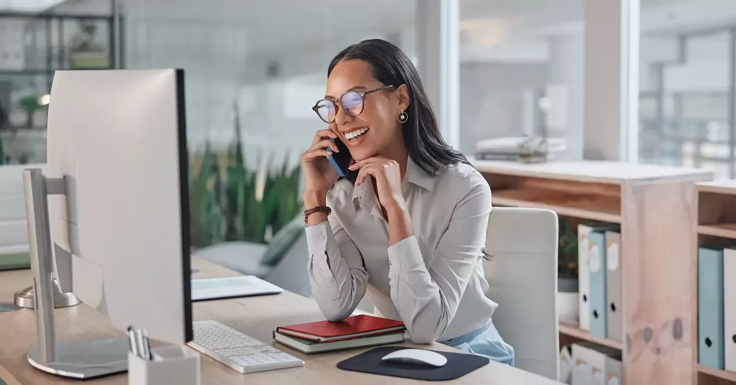 Smiling office worker talking on her phone and using her internet.