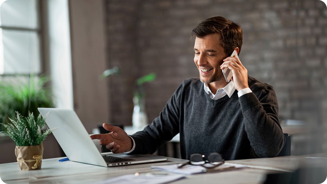Business man uses laptop and phone at desk in office.