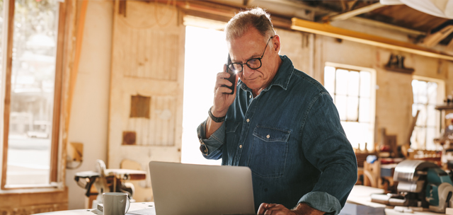 carpenter in his shop using the phone and looking at his laptop