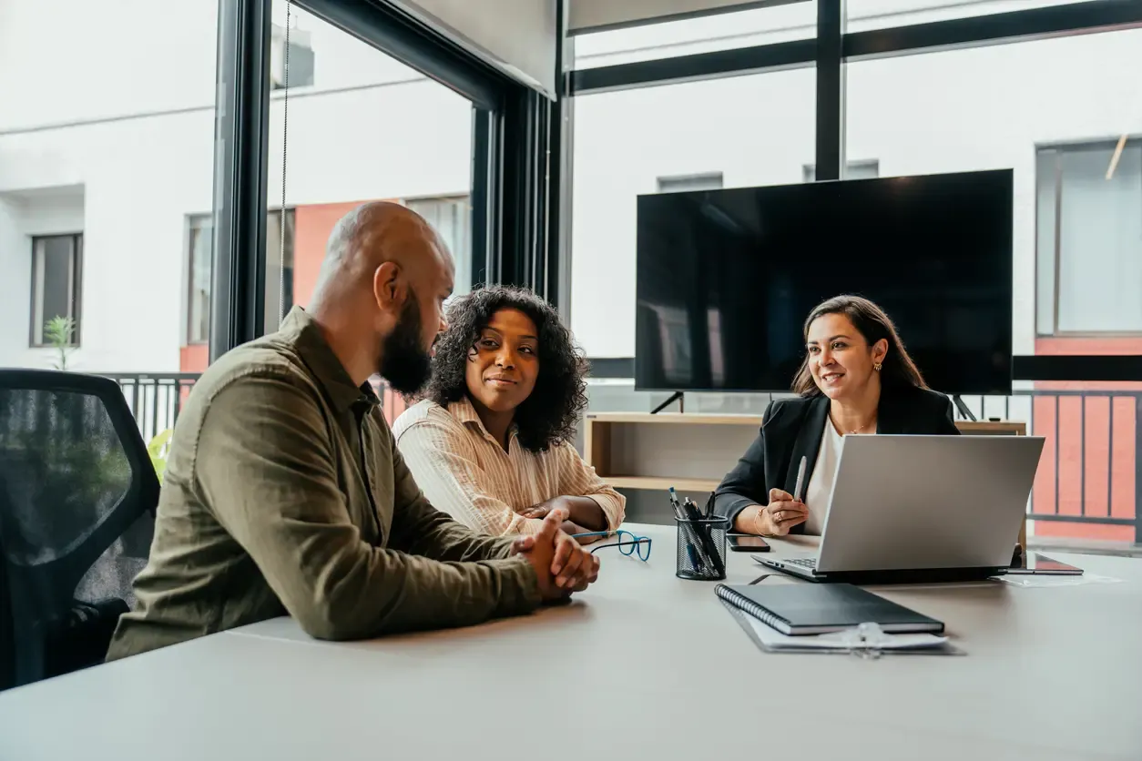 A couple sits across from a smiling advisor with a laptop during a consultation in a modern office.