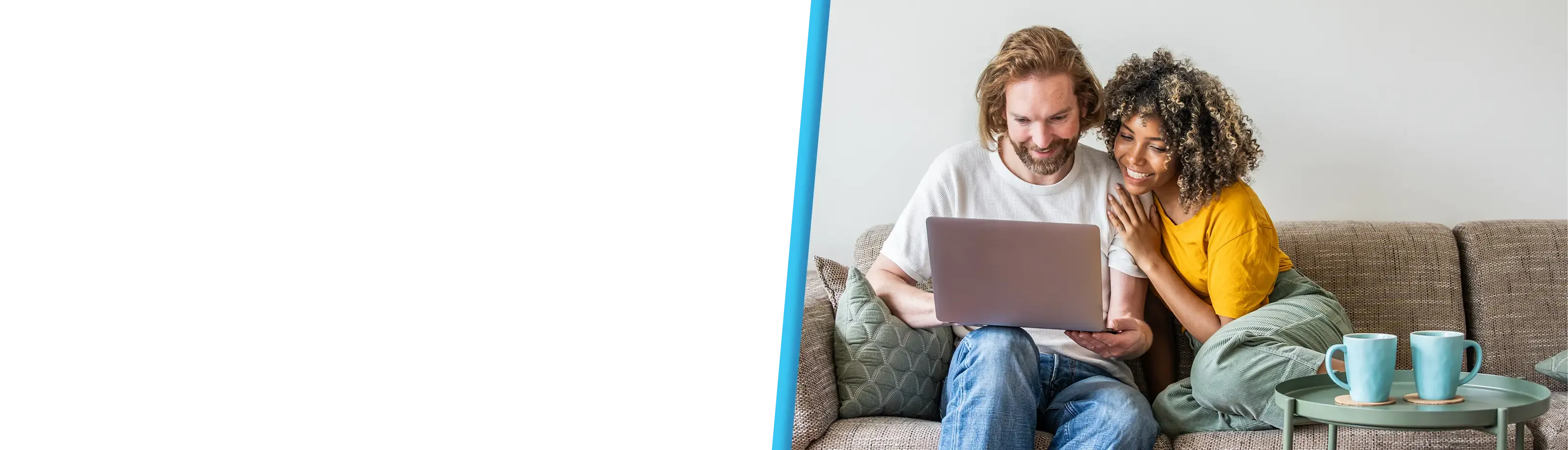 A smiling couple sits close together on a couch, looking at a laptop in a bright living room.