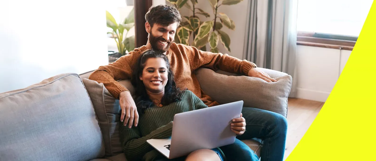 A happy couple sitting together on a grey sofa looking at a laptop.