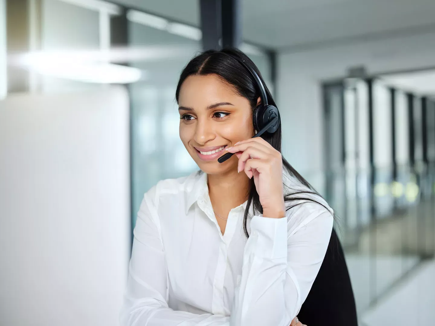 Una sonriente representante femenina de servicio al cliente con auriculares en un entorno de oficina moderno.