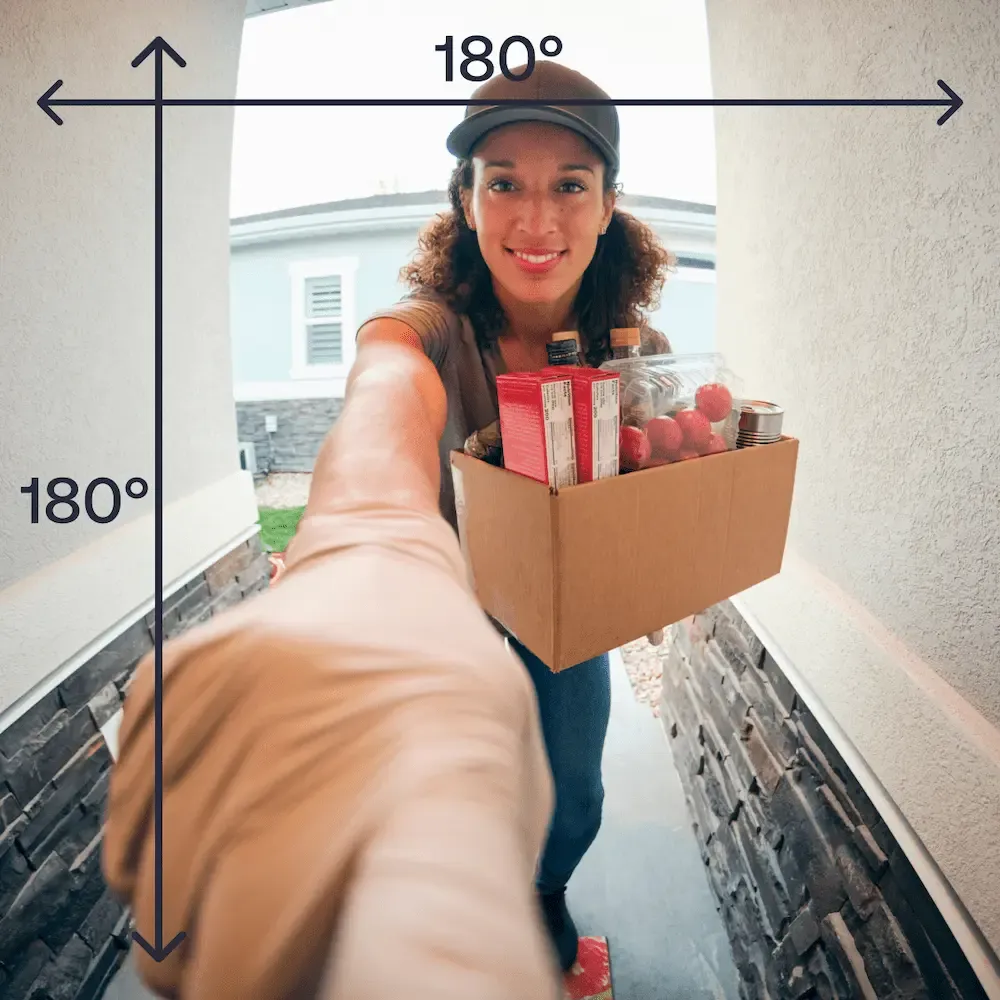 A person in a neon safety vest carrying packages walks up the front steps of a brick house toward an installed Vivint doorbell camera.