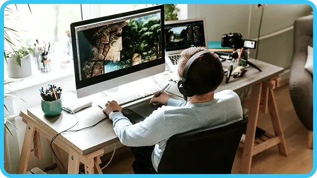 A person wearing headphones uses a graphics tablet at a dual-monitor desk in a home studio.