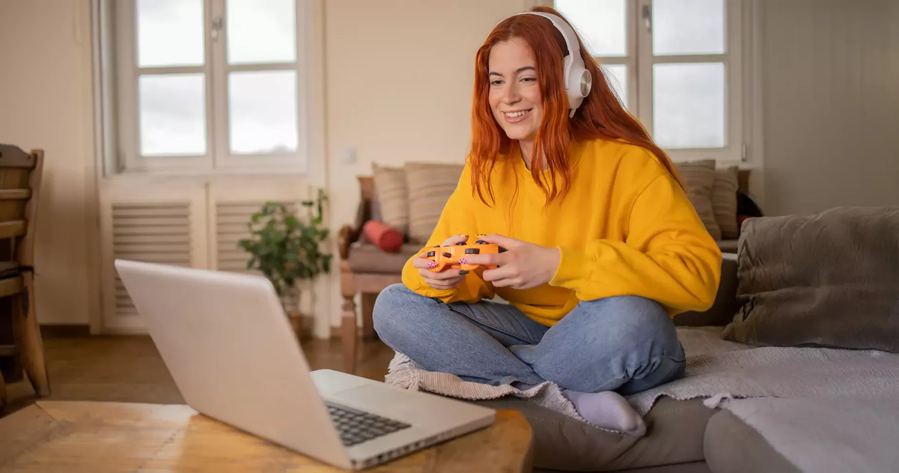 Woman wearing yellow plays video games at home on her laptop.