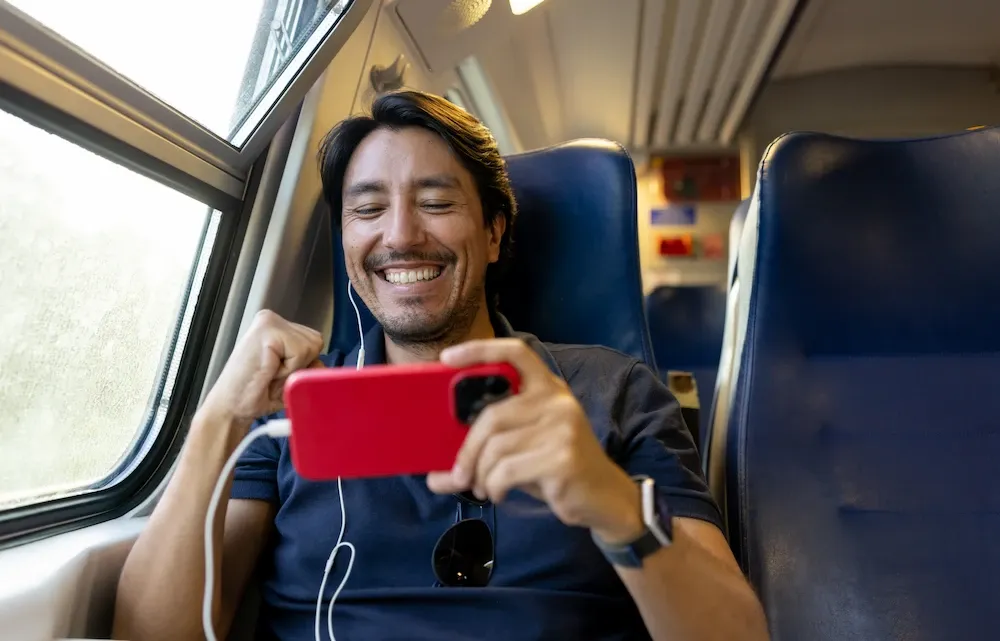 An excited man smiles and pumps his fist while watching media on his smartphone during a train ride.