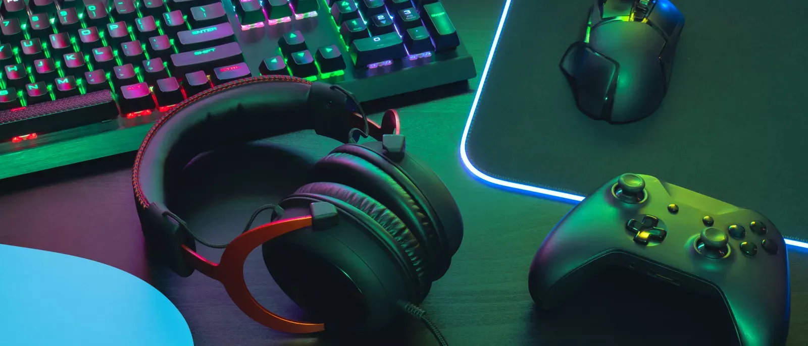Desktop show of gaming headphones, keyboard, mouse, and controller all lit up by neon lights.