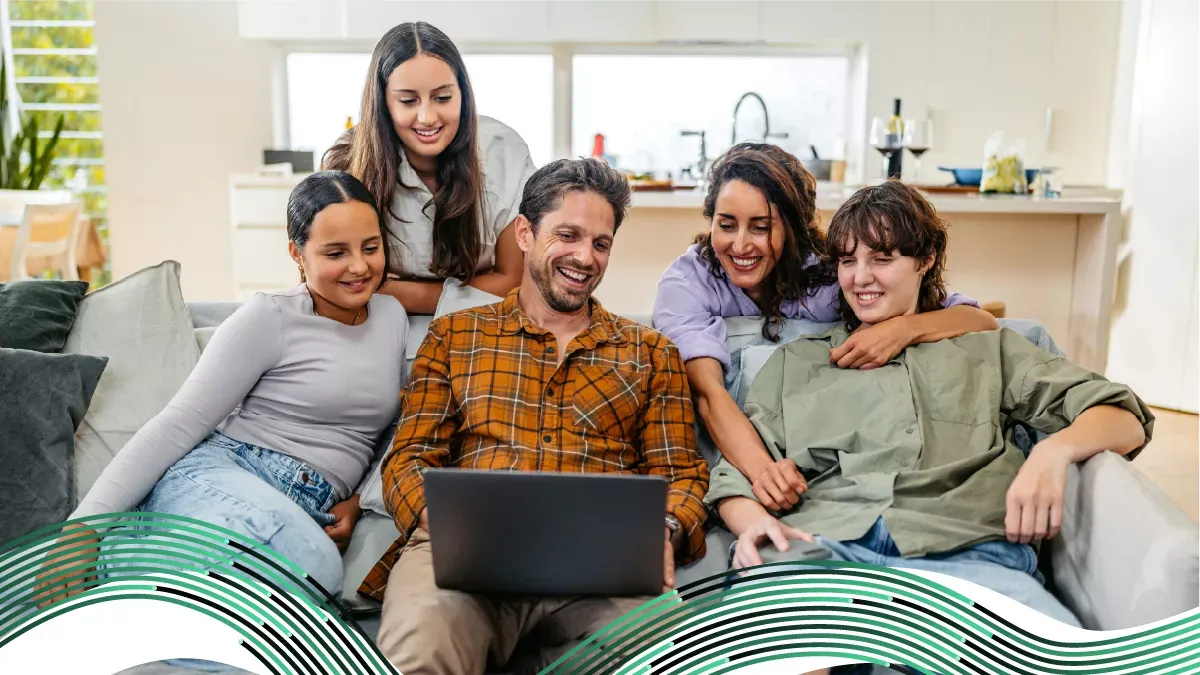 Una familia feliz de cinco personas riendo junta mientras miran una computadora portátil en una sala de estar iluminada.