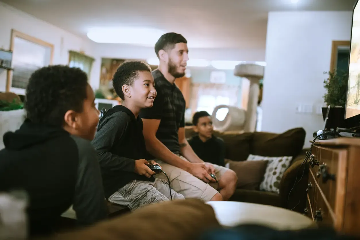 A young man and two children smile while playing video games together on a living room couch.