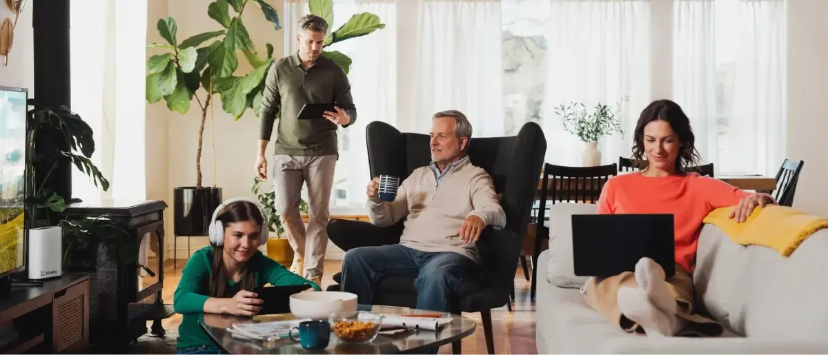 A multi-generational family using various digital devices including laptops and tablets while relaxing together in a bright, modern living room.