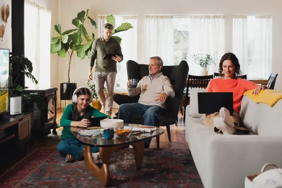 A multi-generational family using various digital devices including laptops and tablets while relaxing together in a bright, modern living room.