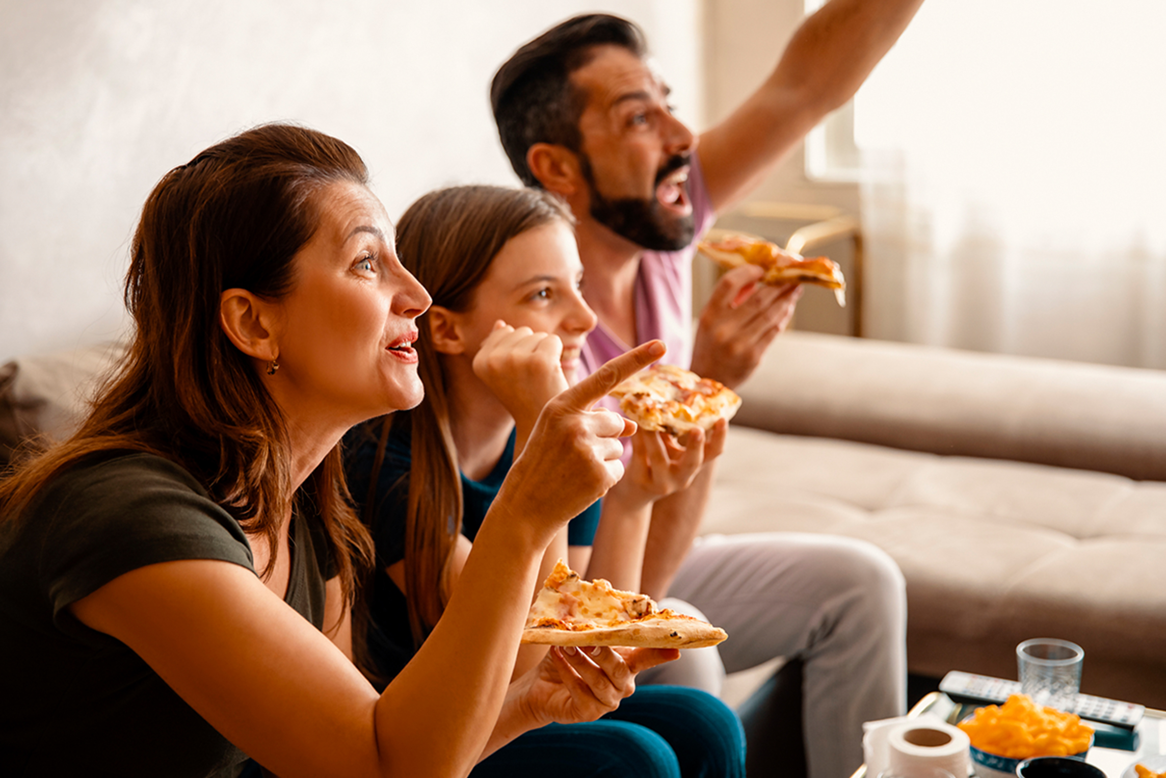 Family eats pizza and watches tv at home.