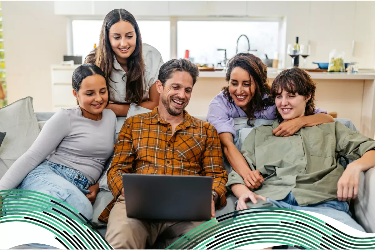 Una familia feliz de cinco personas riendo junta mientras miran una computadora portátil en una sala de estar iluminada.