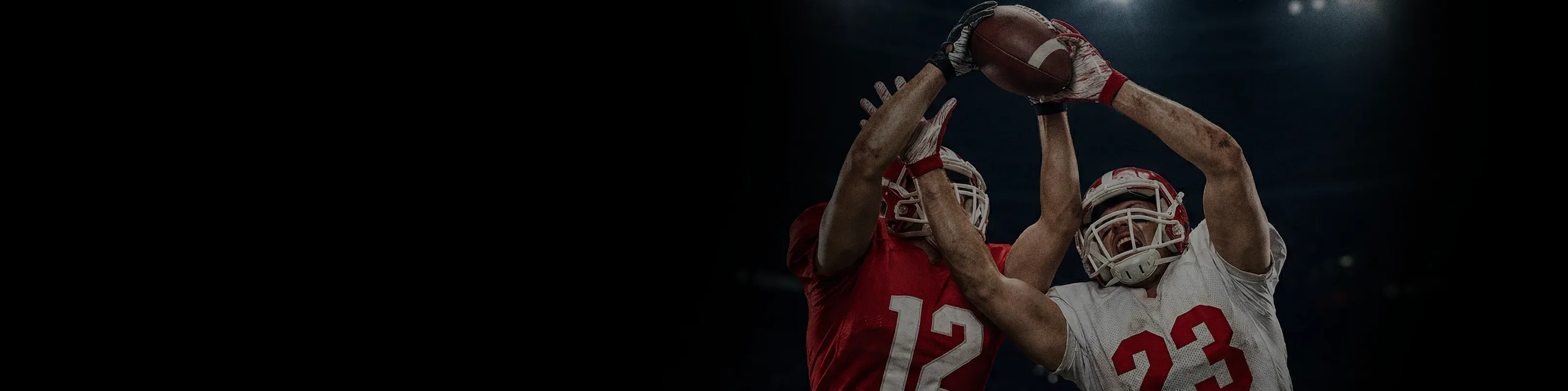 wo football players in red and white uniforms leaping into the air to compete for a catch.