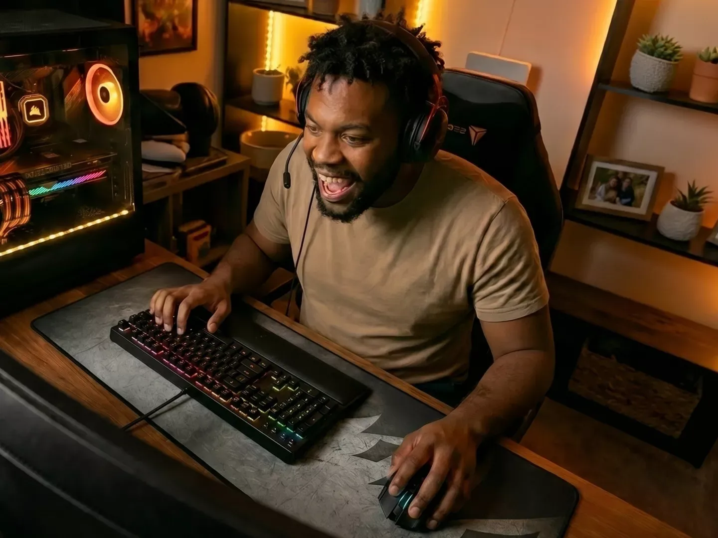 An excited man wearing a headset plays a video game on a high-end desktop computer with colorful lighting.