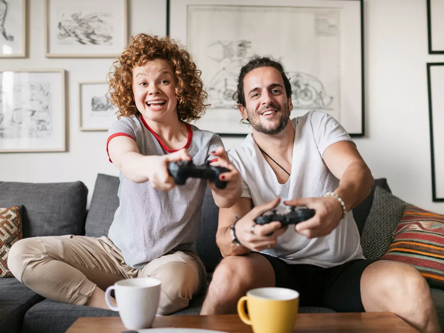 An excited couple sitting on a couch in their living room holding video game controllers.