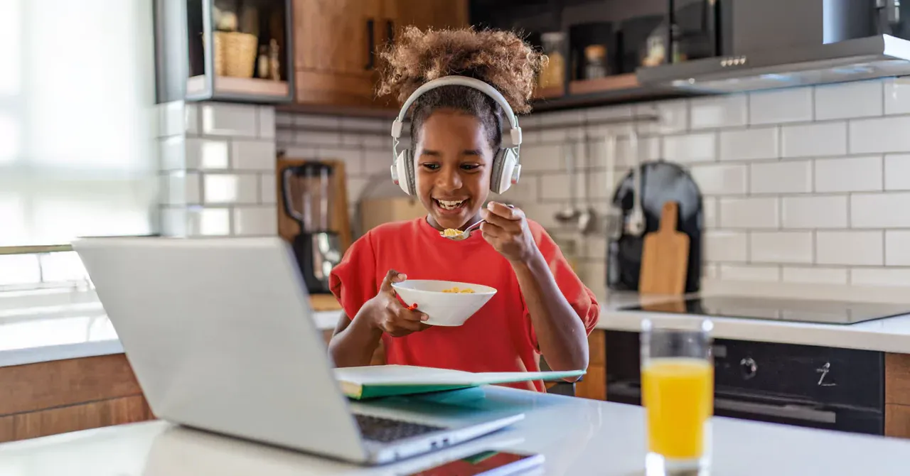 girl watching cartoons on laptop while happily eating her breakfast
