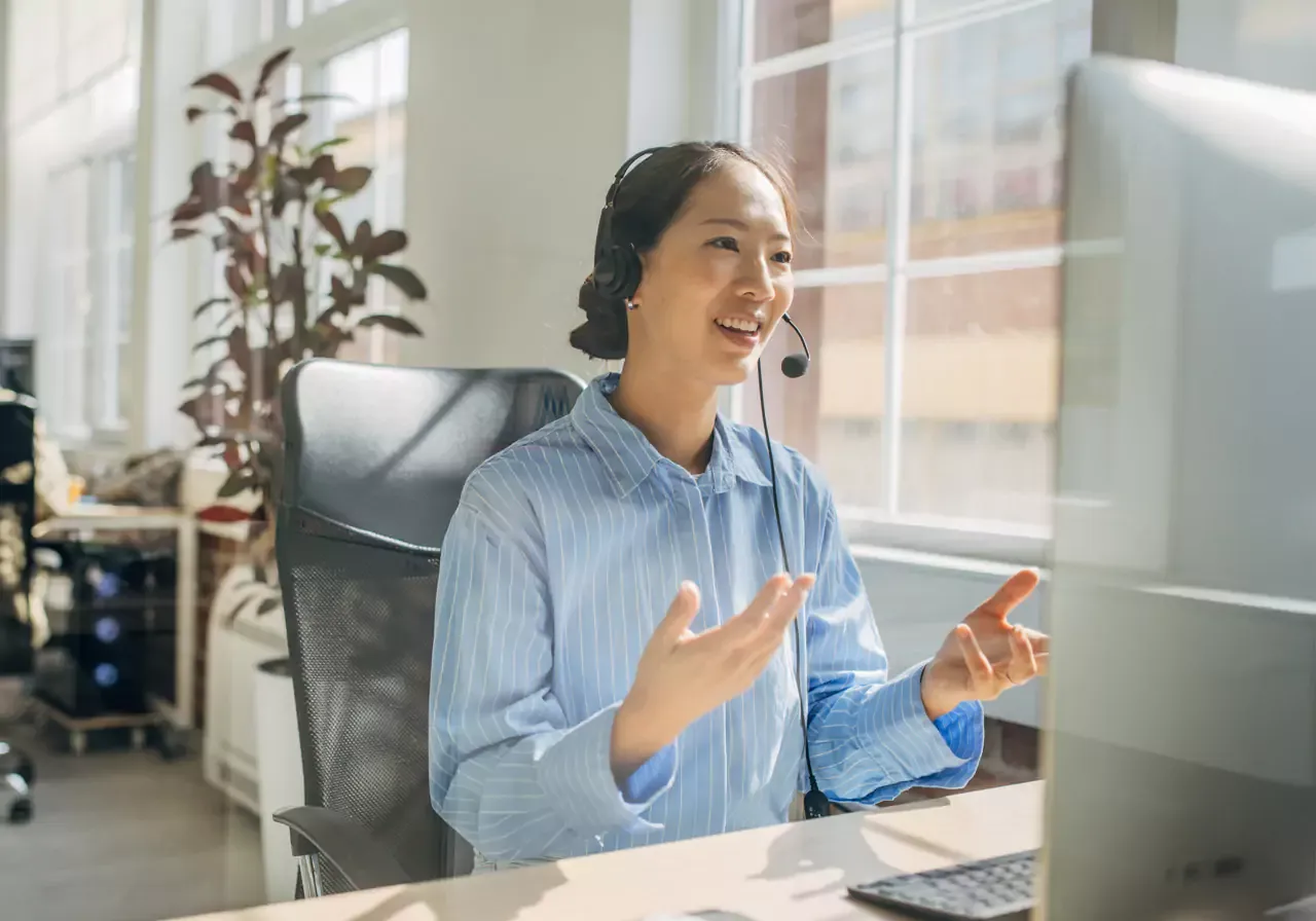 Smiling female customer service agent, helping someone on a call and gesturing with her hands.