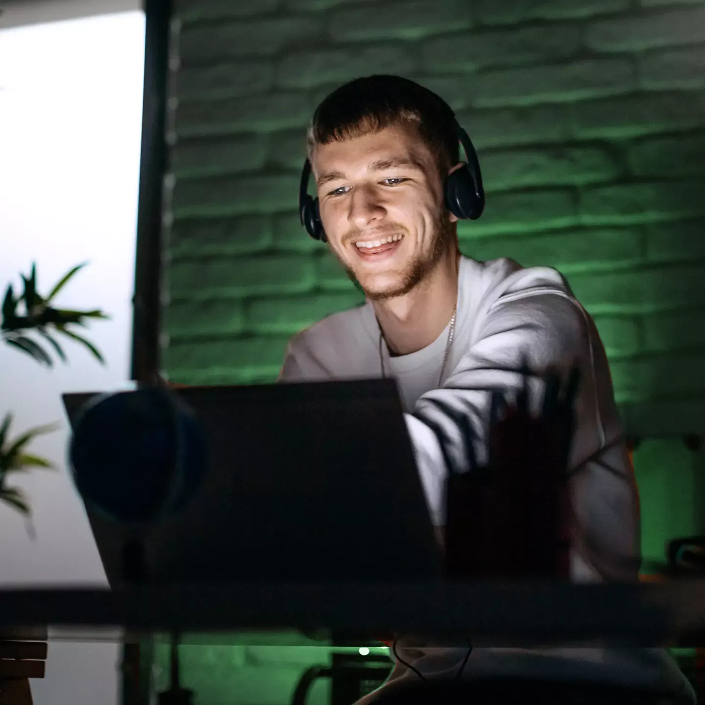 Guy cruising the internet, streaming movies and songs on his laptop, in front of a green neon light.