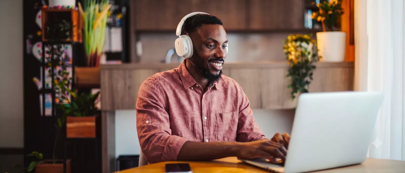 Smiling man working from home on his laptop, and using over ear headphones.