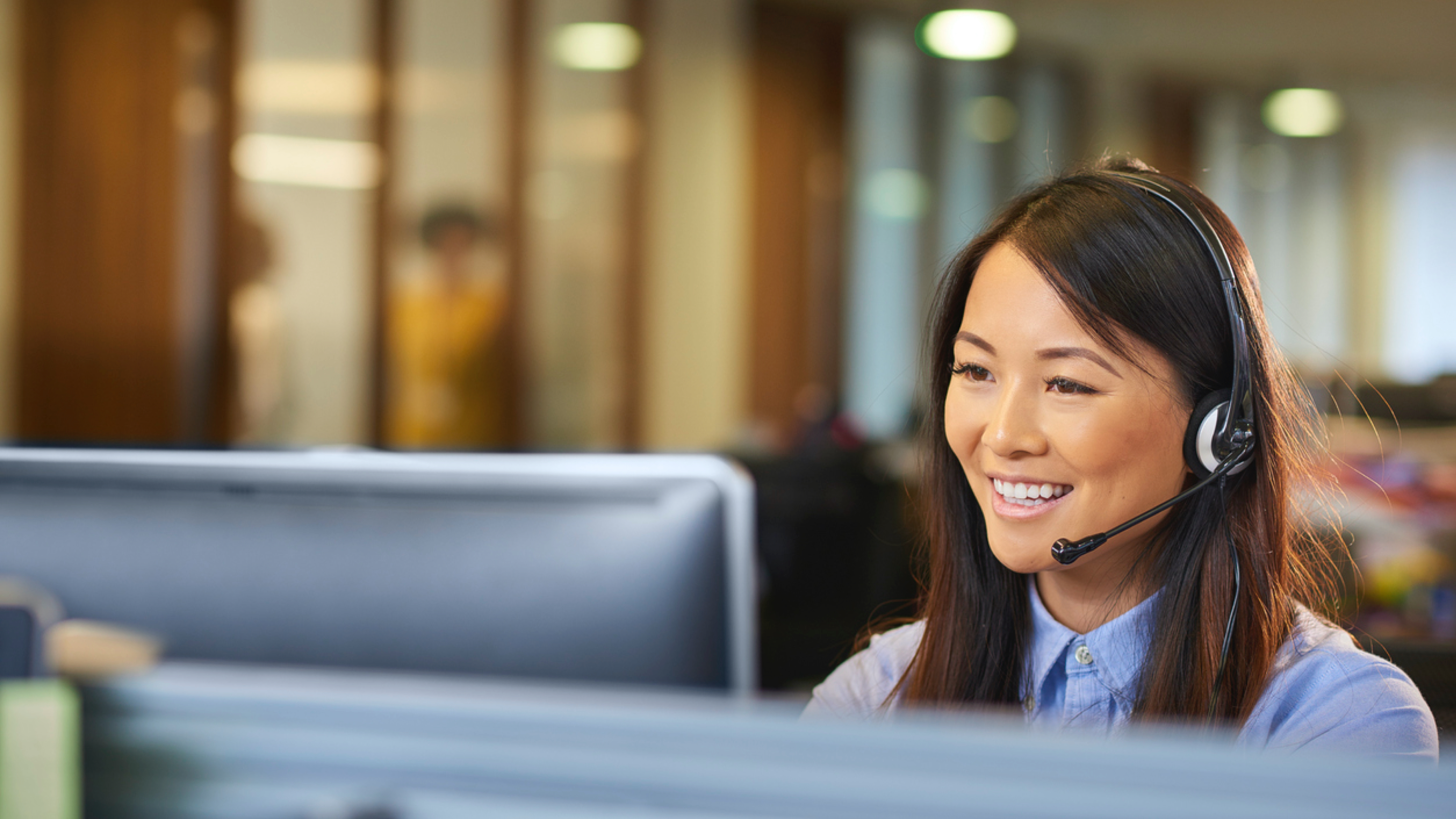 Customer service representative on the phone while wearing headset and sitting at a computer.