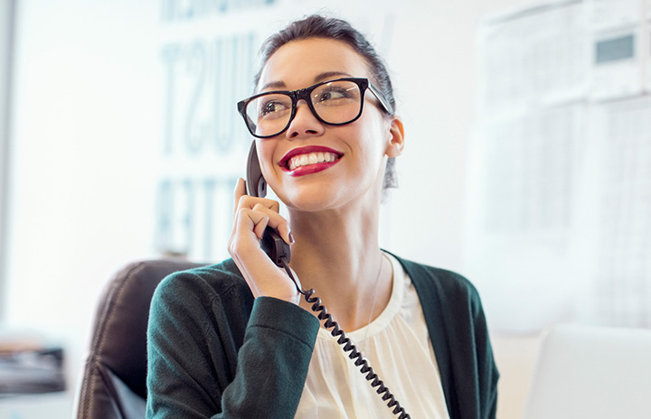 Happy woman talks on business phone at work.