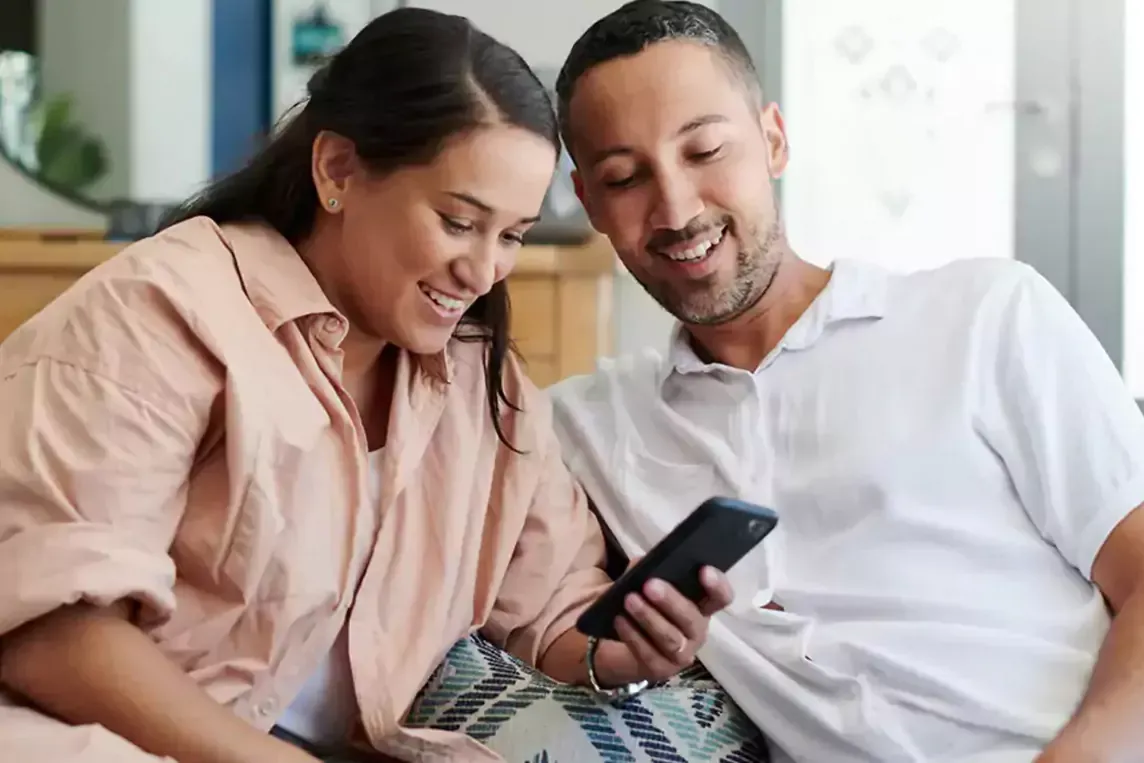 Happy couple uses cell phone in living room.