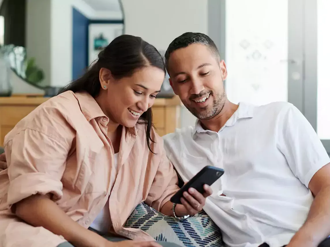 Happy couple uses cell phone in living room.