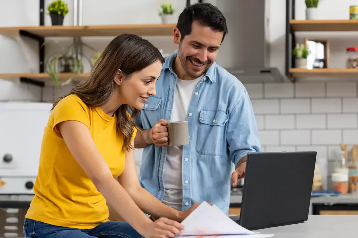 Happy couple uses laptop in kitchen.