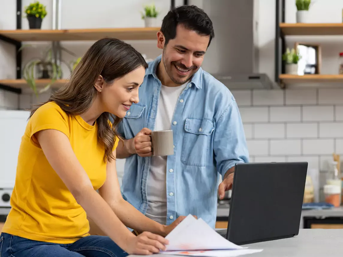 Happy couple uses laptop in kitchen.