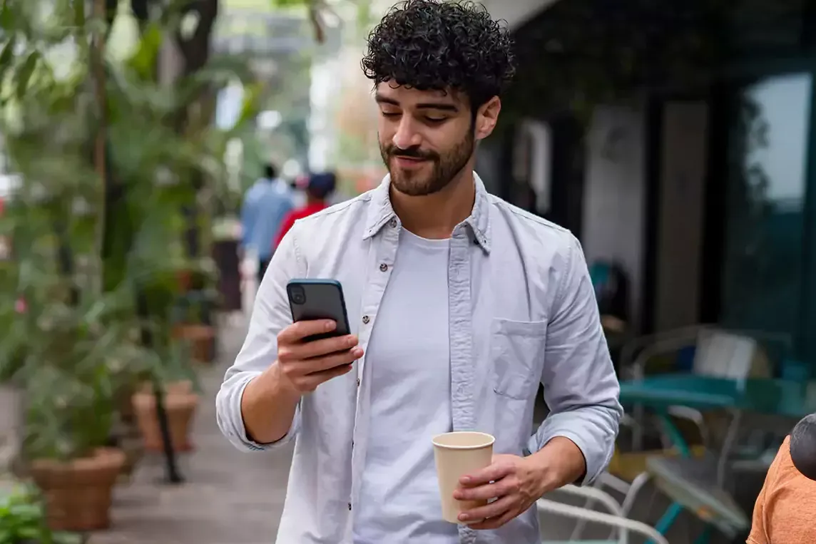 Man uses cell phone outside on the go with coffee.