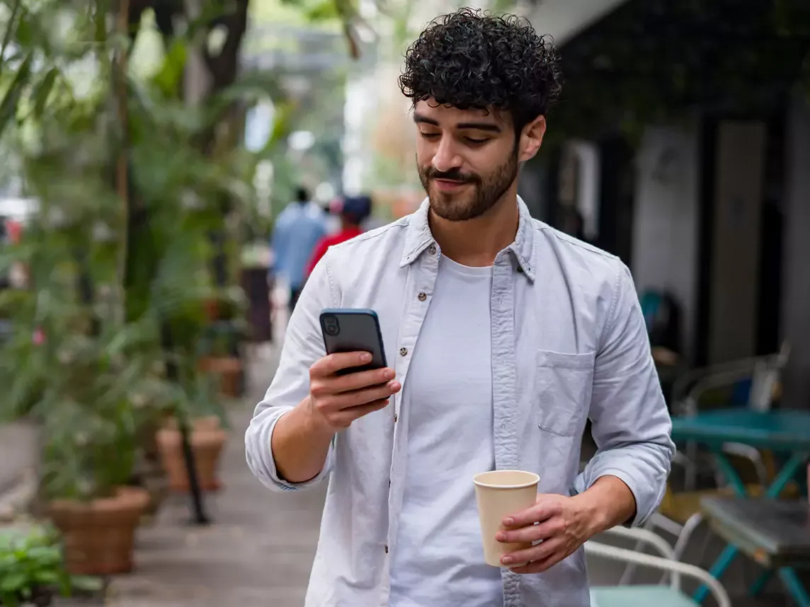 Man uses cell phone outside on the go with coffee.