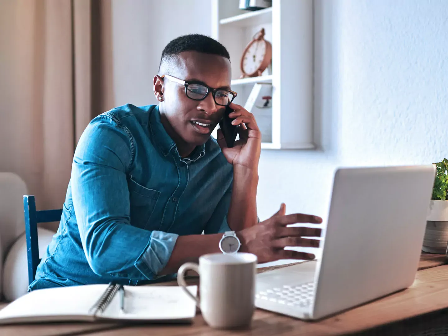 Man in his home office using his laptop, chatting on the phone and getting work done.
