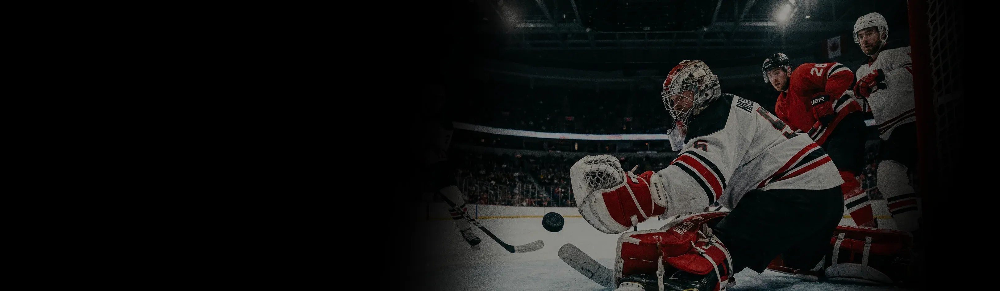 View from inside the net of an ice hockey goalie in white and red gear attempting to block a flying puck during a game.