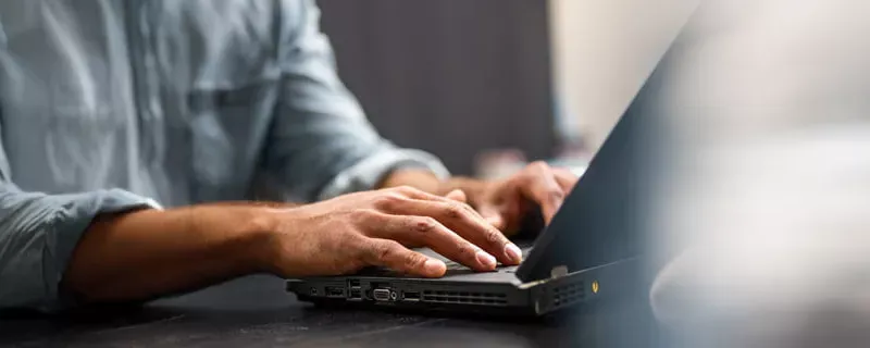 A close-up shot of a person's hands typing on the keyboard of an open black laptop.