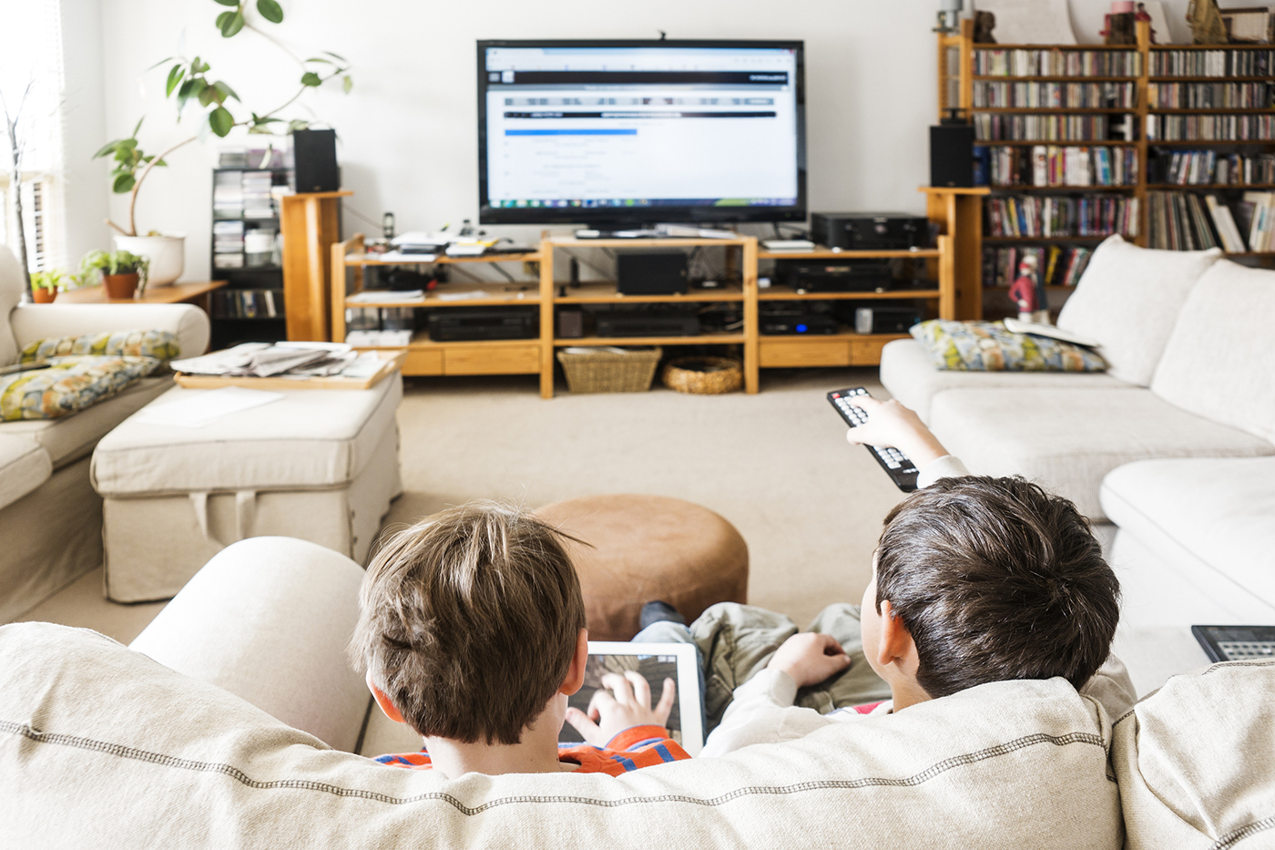 Two kids on couch watching tv and using tablet